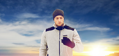 Image showing happy man with earphones and smartphone in winter