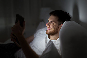 Image showing young man with tablet pc in bed at home bedroom