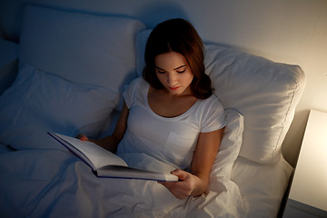 Image showing young woman reading book in bed at night home