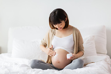 Image showing happy asian pregnant woman applying cream to belly