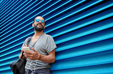 Image showing man with earphones and smartphone over wall
