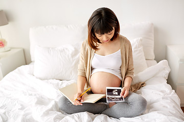 Image showing pregnant woman with fetal ultrasound image at home