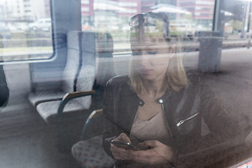 Image showing Young woman traveling by train, using smart phone.