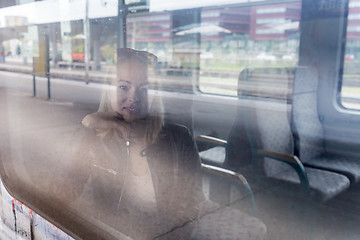 Image showing Young woman traveling by train, looking out window while sitting in train.