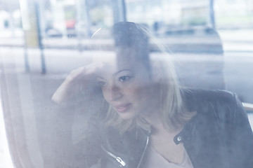 Image showing Young woman traveling by train, looking out window while sitting in train.