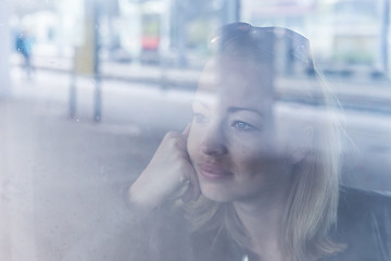 Image showing Young woman traveling by train, looking out window while sitting in train.