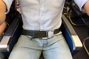 Image showing Male passenger with seat belt fastened while sitting on airplane for safe flight.