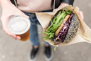 Image showing Female Hands Holding Delicious Organic Salmon Vegetarian Burger and Homebrewed IPA Beer.