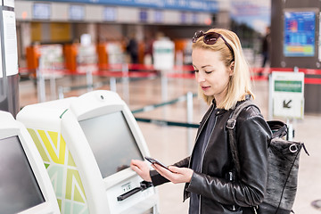 Image showing Casual caucasian woman using smart phone application and check-in machine at the airport getting the boarding pass.