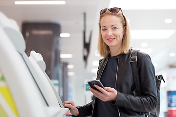 Image showing Casual caucasian woman using smart phone application and check-in machine at the airport getting the boarding pass.