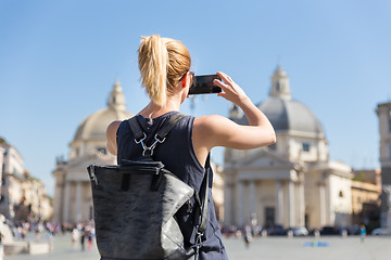 Image showing Female tourist with a fashinable vintage hipster backpack taking photo oof Piazza del Popolo in Rome, Italy by her mobile phone.