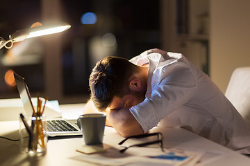 Image showing tired businessman lying on table at night office