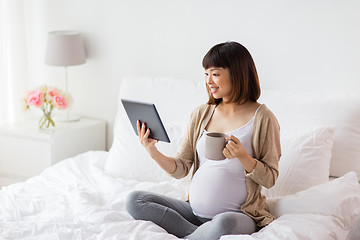 Image showing happy pregnant asian woman with tablet pc at home