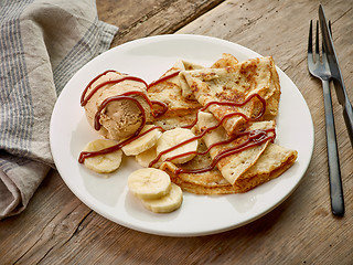 Image showing Crepes with banana and caramel icecream on wooden desk