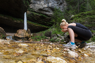 Image showing Active sporty woman drinking water from outdoor stream with her hands.