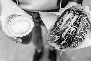 Image showing Female Hands Holding Delicious Organic Salmon Vegetarian Burger and Homebrewed IPA Beer.