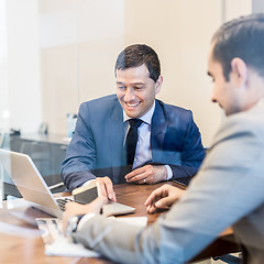 Image showing Two young businessmen using laptop computer at business meeting.