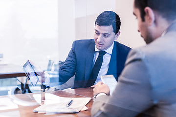 Image showing Two young businessmen using electronic devices at business meeting.