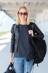 Image showing Portrait of young cheerful female traveler wearing casual clothes carrying heavy backpack and luggage at airport.