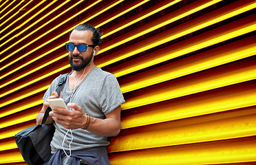 Image showing man with earphones and smartphone over wall