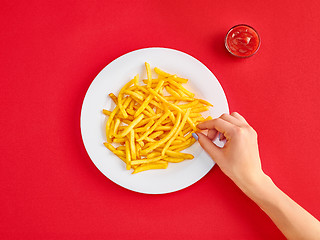 Image showing Young woman eating french fries potato with ketchup in a restaurant