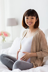 Image showing happy pregnant asian woman sitting in bed at home