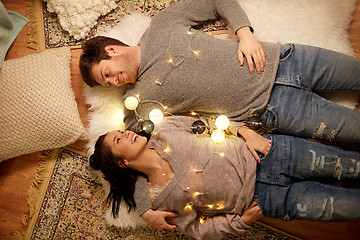 Image showing happy couple with garland lying on floor at home