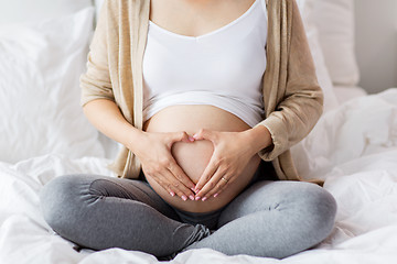 Image showing happy pregnant woman making heart gesture in bed