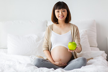 Image showing happy pregnant woman with apple in bed at home