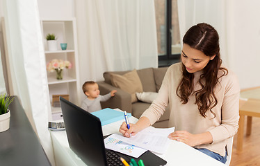 Image showing happy mother with baby and papers working at home