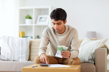 Image showing man with calculator counting money at home