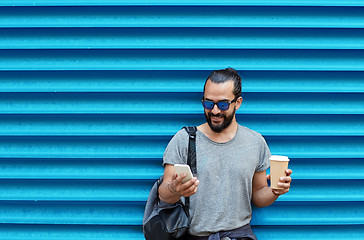 Image showing man with coffee cup and smartphone over blue wall