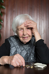 Image showing Elderly woman sitting at the table counting money in her wallet.