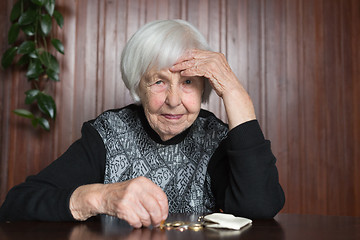 Image showing Elderly woman sitting at the table counting money in her wallet.