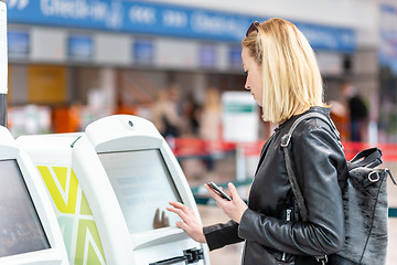 Image showing Casual caucasian woman using smart phone application and check-in machine at the airport getting the boarding pass.