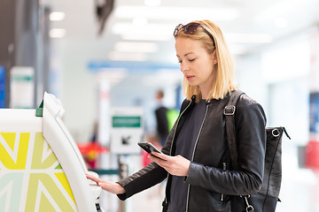 Image showing Casual caucasian woman using smart phone application and check-in machine at the airport getting the boarding pass.