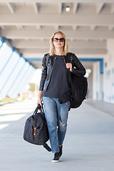 Image showing Portrait of young cheerful female traveler wearing casual clothes carrying heavy backpack and luggage at airport.