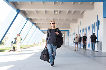 Image showing Portrait of young cheerful female traveler wearing casual clothes carrying heavy backpack and luggage at airport.