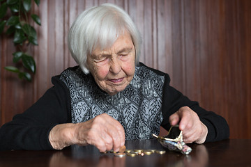 Image showing Elderly woman sitting at the table counting money in her wallet.