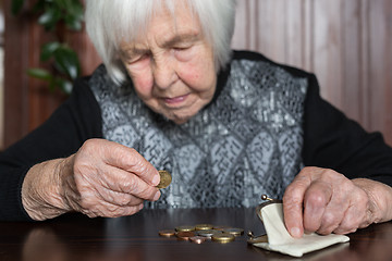 Image showing Elderly woman sitting at the table counting money in her wallet.