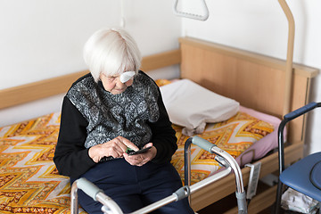 Image showing Lonley elderly 95 years old woman sitting at the bad using modern mobile phone.