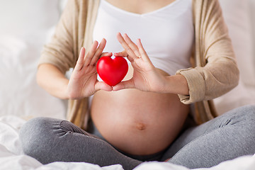 Image showing close up of pregnant woman with red heart in bed