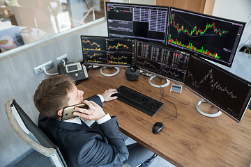 Image showing Over the shoulder view of stock broker trading online, talking on mobile phone.