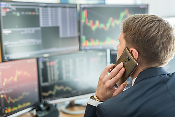 Image showing Over the shoulder view of stock broker trading online, talking on mobile phone.