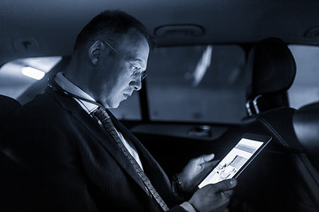 Image showing Businessman with a digital tablet sitting in the back seat of a car