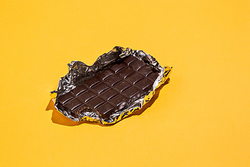 Image showing Bitten Chocolate bar in foil isolated on yellow background.