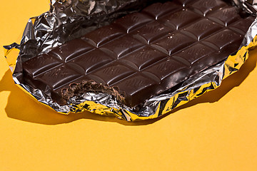 Image showing Bitten Chocolate bar in foil isolated on yellow background.