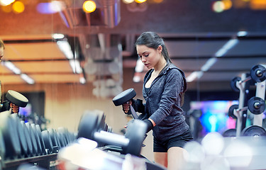 Image showing young woman choosing dumbbells in gym