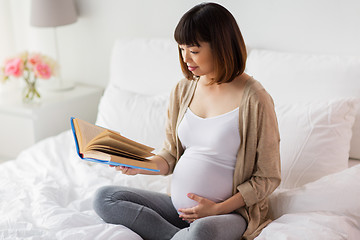 Image showing happy pregnant asian woman reading book at home