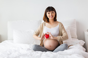 Image showing happy pregnant asian woman with red heart in bed